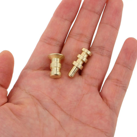 Gold-finish metal table pins and dowels set for furniture joints and desk assembly alignment held in hand.