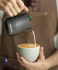 12 Oz Stainless Steel Milk Frothing Pitcher For Espresso And Latte Art Black Round Spout Milk Jug pouring milk into coffee
