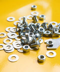 100 Piece Set Of 1/4 Inch Flat Washers Crafted From Top Shelf 316 Stainless Steel For Nailing Down Bolts And Screws With A Solid Marine Grade Feel Perfect For Daily Grind Tasks And Outdoor Builds scattered among screws and nuts on a yellow surface.
