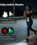 Woman jogging at night with clip-on running light showing 4 adjustable modes on track. Battery life displayed.