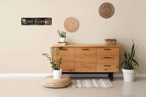 Snag This Sick Vintage Metal Tin Sign Keep It Weird Wall Decor Plaque 4x16 Inches above a wooden side table with plants.