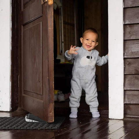 Child standing near a door secured by a 2 Piece Rubber Door Wedge With Stainless Steel Core Non Slip Door Stopper