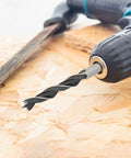 Close-up of a drill with a bit on chipboard, part of the Eight Piece Wood Drill Bits Set Carbon Steel Brad Point Kit For Woodworking.