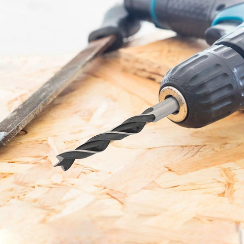Close-up of a drill with a bit on chipboard, part of the Eight Piece Wood Drill Bits Set Carbon Steel Brad Point Kit For Woodworking.