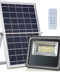 JUDYSSY 30W Led Solar Powered Flood Lights with Remote Control next to solar panel and remote, Ip66 Waterproof