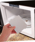 Hand holding a mica sheet in front of an open microwave, 10 Pack High Temperature Mica Sheets For Microwave Waveguide Covers And Oven Repairs Durable Heat Insulation Panels Wide Brand Compatibility DIY Microwave Repair Kit And Accessories.