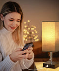 Woman using phone next to small nightstand lamp with USB, black shade for end tables, set of 2 bedside lamps with dual USB ports