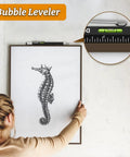 Woman hanging seahorse art using a level tool with focus on bubble leveler.