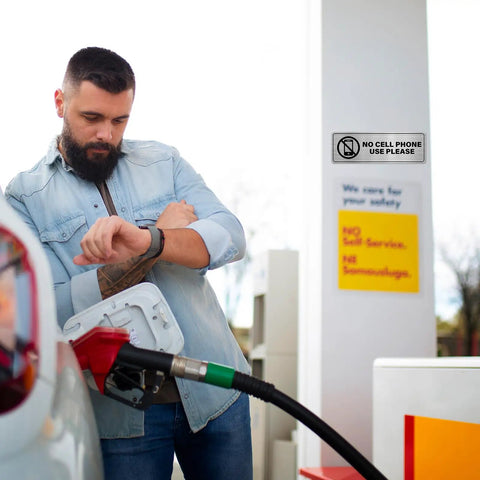 Person at fuel pump with 'No Cell Phone Use Please' sign visible on wall