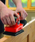 User operating a Badass Compact Electric Orbital Sander on a wooden door for smooth surface finishing.