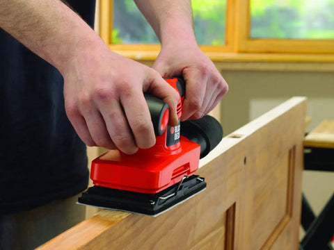 User operating a Badass Compact Electric Orbital Sander on a wooden door for smooth surface finishing.