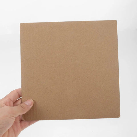 Hand holding 12 pack corrugated paper moving box filler sheet for quick protective base and waste reduction, 20x20cm cardboard pad