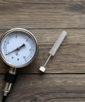 Pressure gauge and tool on wooden surface, showing measurements and hardware, no visible branding.