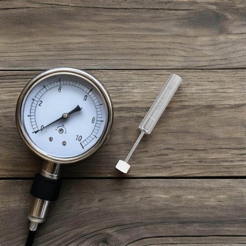 Pressure gauge and tool on wooden surface, showing measurements and hardware, no visible branding.