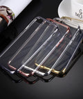 Four transparent phone cases with metallic edges in black, gold, silver, and rose gold on a reflective black surface.
