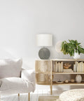 Round Terracotta Table Lamp With Canvas Shade In Distressed Grey Finish on bookshelf with plants and books, cozy living room setting