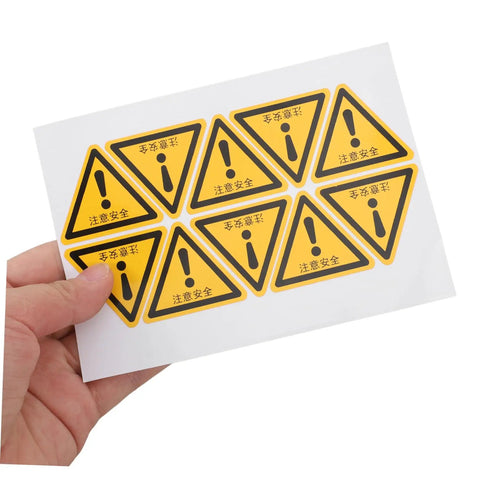 Hand holding sheet of 24 Pcs Machine Warning Labels Safety Sign Stickers Caution Decals For Equipment Factory Indoor Outdoor Use