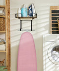 Laundry room with wall mounted ironing board hanger and iron holder with large black wooden base basket, pink board visible.