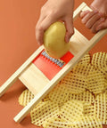 Crinkle cutter with wooden guide slicing a potato into waffle-cut chips; red blade insert visible.