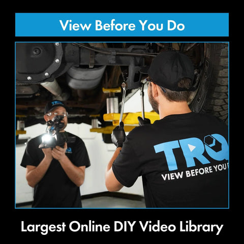 Two mechanics inspecting undercarriage with wrench and flashlight, TRQ shirts, in professional garage setting.