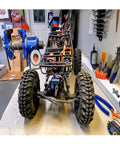 RC car chassis with blue frame and large off-road tires on a workbench; exposed wiring and components.