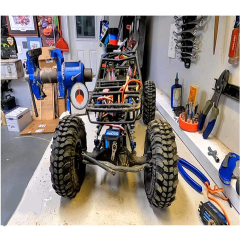 RC car chassis with blue frame and large off-road tires on a workbench; exposed wiring and components.