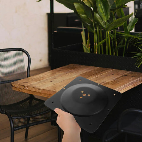 Hand holding a black metal Premium Furniture Leg Connector Mounting Plate near a wooden table for DIY projects.