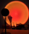Sunset Lamp With Remote LED RGB Projection Night Light creating a vibrant multicolor sunset glow behind decor items on a table.