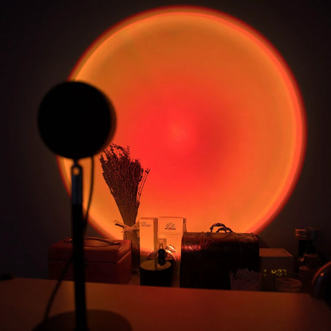 Sunset Lamp With Remote LED RGB Projection Night Light creating a vibrant multicolor sunset glow behind decor items on a table.