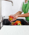 Person washing fruit in kitchen sink with Ten-Piece Water Absorbent Mats 14 By 16 Inches Wringable Reusable Absorbing Pads on counter.