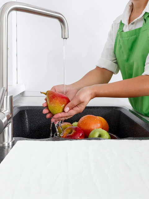 Person washing fruit in kitchen sink with Ten-Piece Water Absorbent Mats 14 By 16 Inches Wringable Reusable Absorbing Pads on counter.