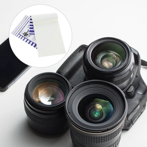 Two white lens-cleaning paper booklets (10x15 cm) beside camera lenses