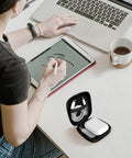 Carry Anywhere EVA Earbud Case With Carabiner on desk beside person using tablet, slim gear pouch open showing space for earphones and USB drives