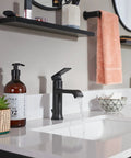 Modern bathroom sink setup with a matte black faucet, soap dispenser, and pink towel on a rod above a white countertop.