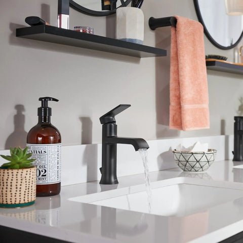 Modern bathroom sink setup with a matte black faucet, soap dispenser, and pink towel on a rod above a white countertop.