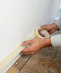 Person applying Economy Masking Tape Three Quarters Inch By Sixty Yards General Purpose Crepe Paper Backing on floor edge for sealing