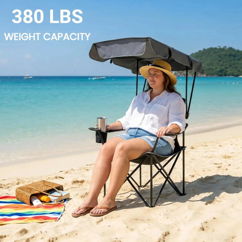 Person sitting on oversized camping chair with adjustable canopy on a beach. Chair has 380 lbs capacity and padded armrests.