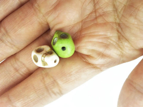 Close-up of two mixed color turquoise skull head spacer beads for DIY jewelry making on a hand, part of a pack of 50, tiny skull shape.