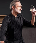 Heavy Duty Chef Coat With Chest And Sleeve Pocket Plus Hella Breathable Fabric That Keeps You Cool In The Heat Top Drawer Restaurant Cook Uniform worn by a chef holding a spice jar.