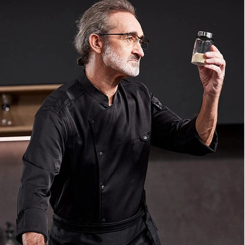 Heavy Duty Chef Coat With Chest And Sleeve Pocket Plus Hella Breathable Fabric That Keeps You Cool In The Heat Top Drawer Restaurant Cook Uniform worn by a chef holding a spice jar.