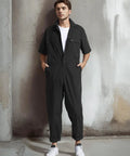 Lightweight Mens Short Sleeve Coveralls And Mechanic Work Jumpsuit Featuring Deep Cargo Pockets Woven From Breezy Summer Twill Cotton Blend For Tough Job Sites And The Daily Grind Low Key Comfy Shop Romper displayed on a model against a textured wall.