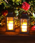 Two Pack Lit Solar Powered Outdoor Hanging Lanterns With Waterproof LED Flickering Flameless Candles in garden setting