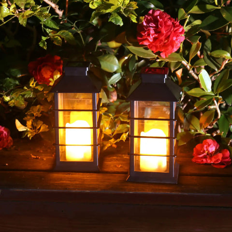 Two Pack Lit Solar Powered Outdoor Hanging Lanterns With Waterproof LED Flickering Flameless Candles in garden setting