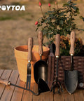 Five Piece Garden Tool Set With Stainless Steel Heads And Ergonomic Walnut Handles displayed on wooden table near potted plants.