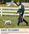 Person walking a dog with blue mesh bag on grass near dog agility course