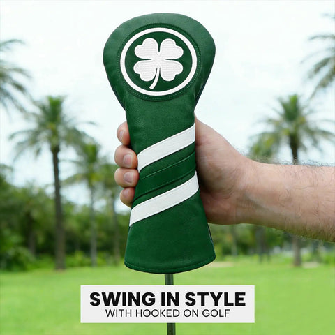 Hand holding a green leather golf club head cover with clover emblem on a golf course background.