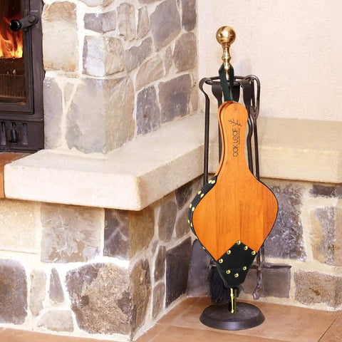 Badass Heavy Duty Oak Wood Fire Bellow For Starting Campfires And Grilling Coals Fast With A Dope Grip resting beside a fireplace.