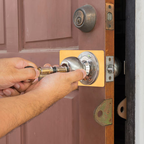 Hands installing Two Pack Stainless Steel Door Lock Reinforcement Plates With Adhesive Tape Gold Finish on wooden door.