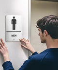 Two Piece ADA Restroom Signs For Business Men's And Women's Bathroom Sign Set In Silver Brushed Aluminum Raised Braille Self Adhesive 9 By 6 Inches Durable, man installing men's sign