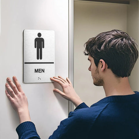 Two Piece ADA Restroom Signs For Business Men's And Women's Bathroom Sign Set In Silver Brushed Aluminum Raised Braille Self Adhesive 9 By 6 Inches Durable, man installing men's sign